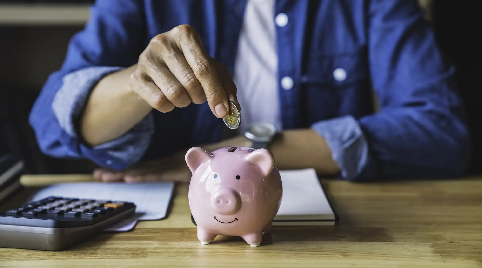 A woman putting money in a piggy bank to save for a mortgage downpayment.