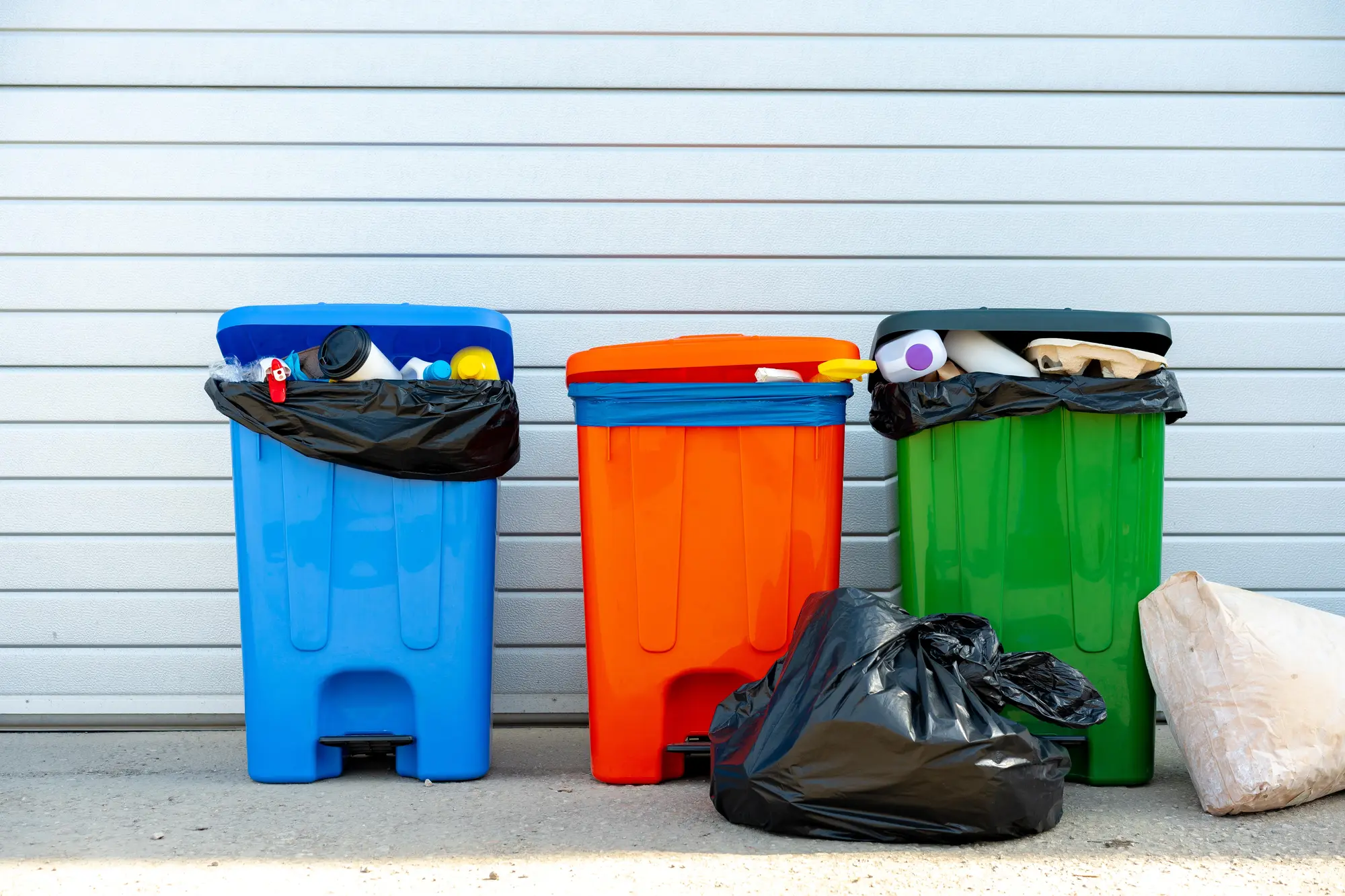 Three trash cans outside of a house for sale.